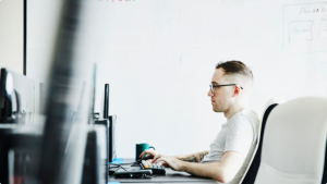 Person sitzt am Schreibtisch und blickt auf den Computerbildschirm 